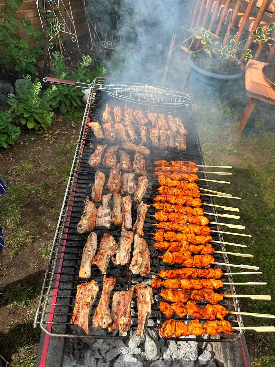Chicken and lamb shish cooking over a charcoal grill in a garden